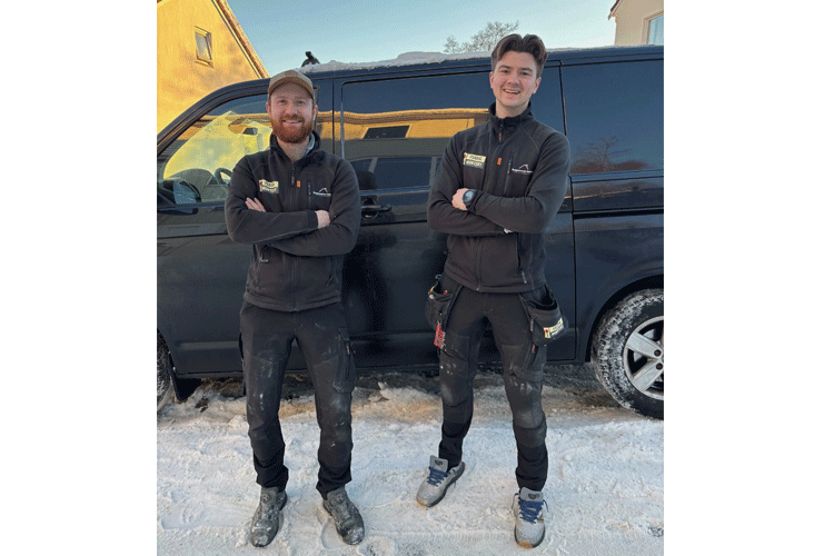 To personer i arbeidsklær står foran en svart varebil på snødekt bakke.