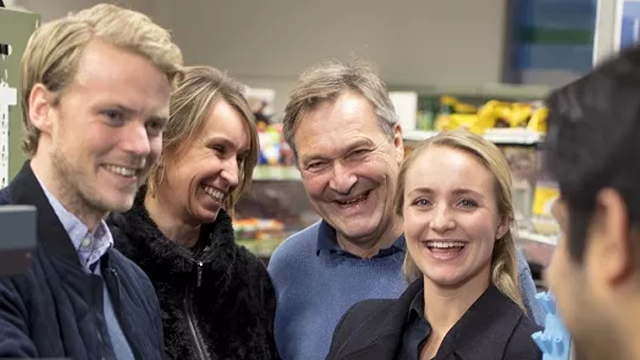 Fire glade mennesker smiler og snakker sammen i en butikk, omgitt av varer på hyllene.