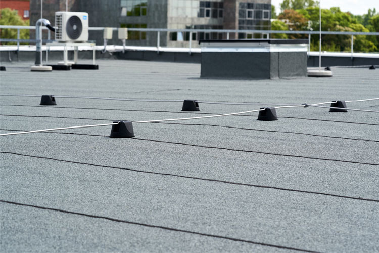 Tak med svart takbelegg og flere små festepunkter, samt en ventilasjonskanal og klimaanlegg i bakgrunnen.