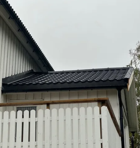Tak med svarte takstein på en bygning, med en hvit plankehekk i forgrunnen.