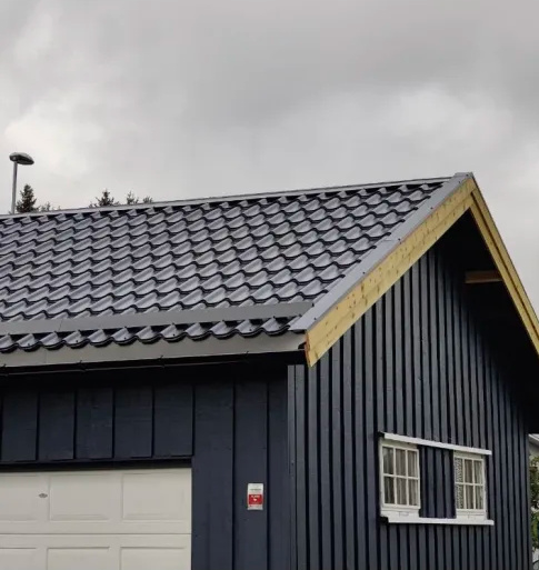 Tak på en moderne, mørkeblå hytte med takstein, under en grå himmel.