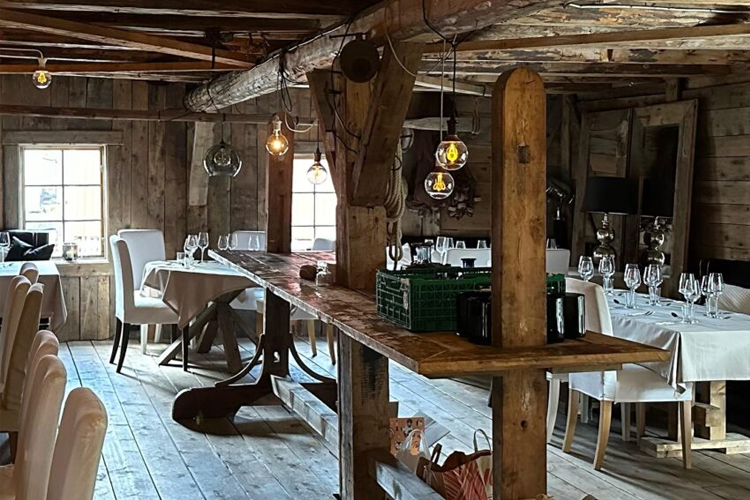 Koselig restaurantinteriør med trevegger, borddekorasjoner og lys i en rustikk atmosfære.