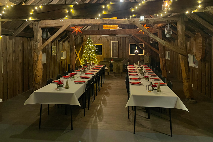 En koselig spisestue med juledekorasjoner, langbord dekket med røde servietter og en juletre i bakgrunnen.