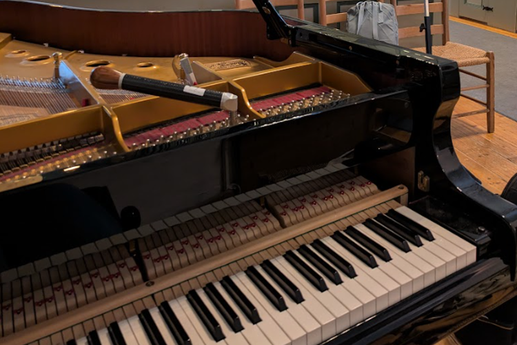 Nærbilde av et svart piano med synlige tangenter og innvendige strenger, plassert i et rom med treverk.