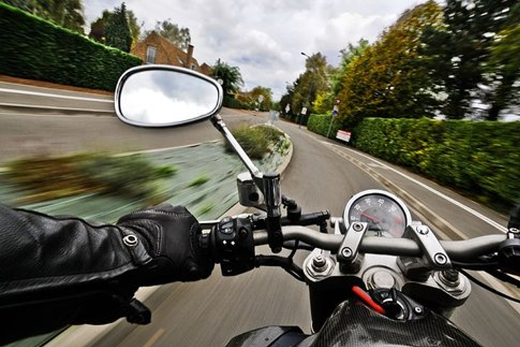 En motorsykkel som kjører raskt på en svingete vei med grøntområder langs kanten.