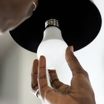 En person skifter en lyspære i en lampe med svart skjerm.