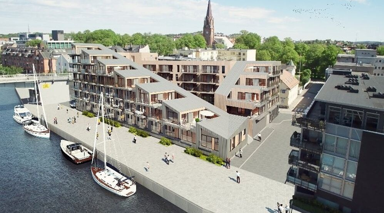 Moderne leilighetskompleks ved elven med båter og en kirke i bakgrunnen, omgitt av grøntområder.