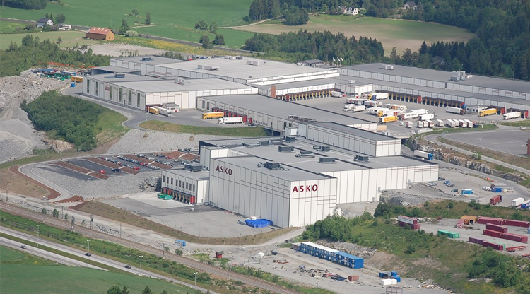 Oversiktsbilde av et industriområde med flere lagerbygninger og lastebiler på en solfylt dag.