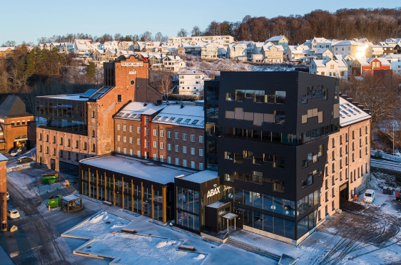 Moderne bygning med glassfasade og snødekt område, omgitt av boliger og trær i bakgrunnen.