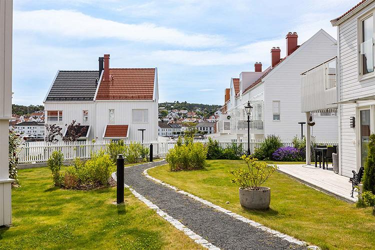 En koselig hage med stier, hvite hus med tak i rødt og grått, og en vakker utsikt over vannet.