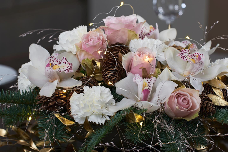En vakker blomsterdekorasjon med roser, orkideer, nelliker og granbar, pyntet med lys og kongler.