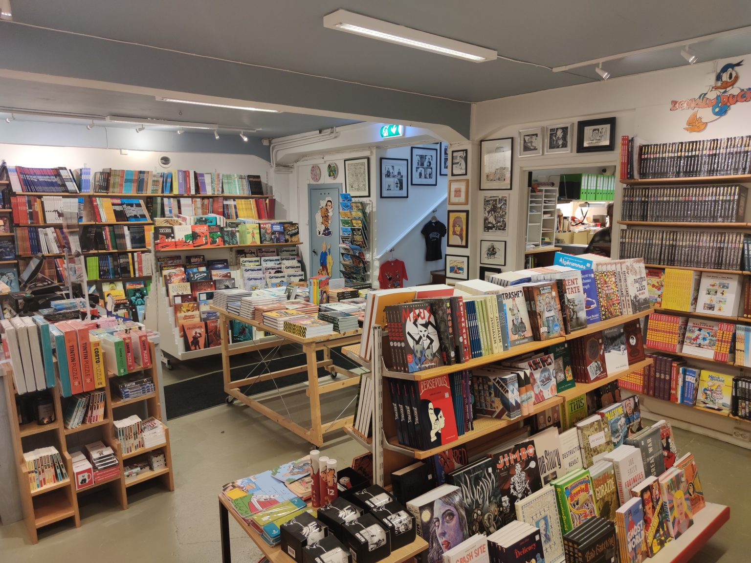 En koselig bokhandel med hyller fylt med bøker, spill og kunstverk, samt en innbydende atmosfære.