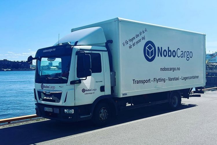 Lastebil fra Nobocargo parkert ved vannkanten, med logo og kontaktinformasjon synlig på siden.