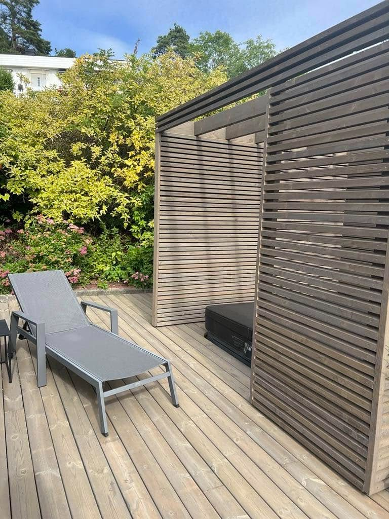 En solstol og en moderne pergola i en hage med grønne planter og blomster.