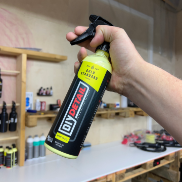 Hånd som holder en sprayflaske med bilpleieprodukt fra DIY Detail i en verkstedsetting.