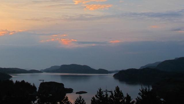 En vakker solnedgang over en rolig fjord med fjell og trær i forgrunnen.