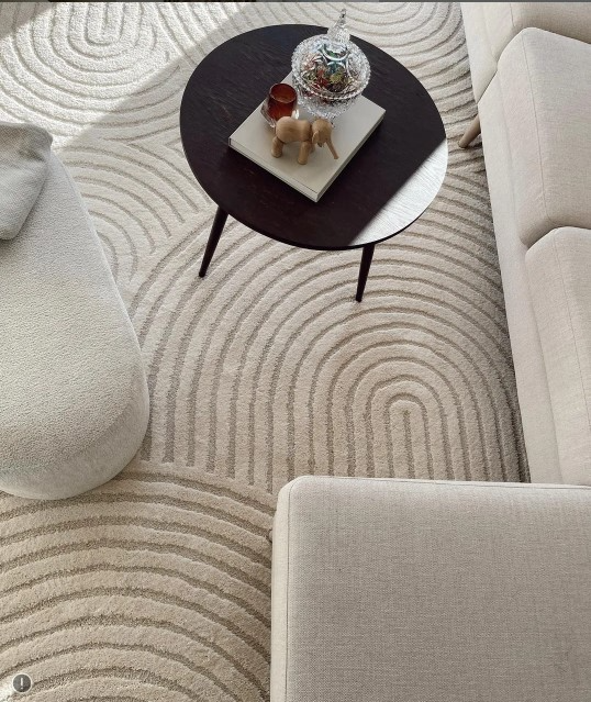 Lys stue med en moderne sofa, et rundt bord og et teppe med bølgemønster.