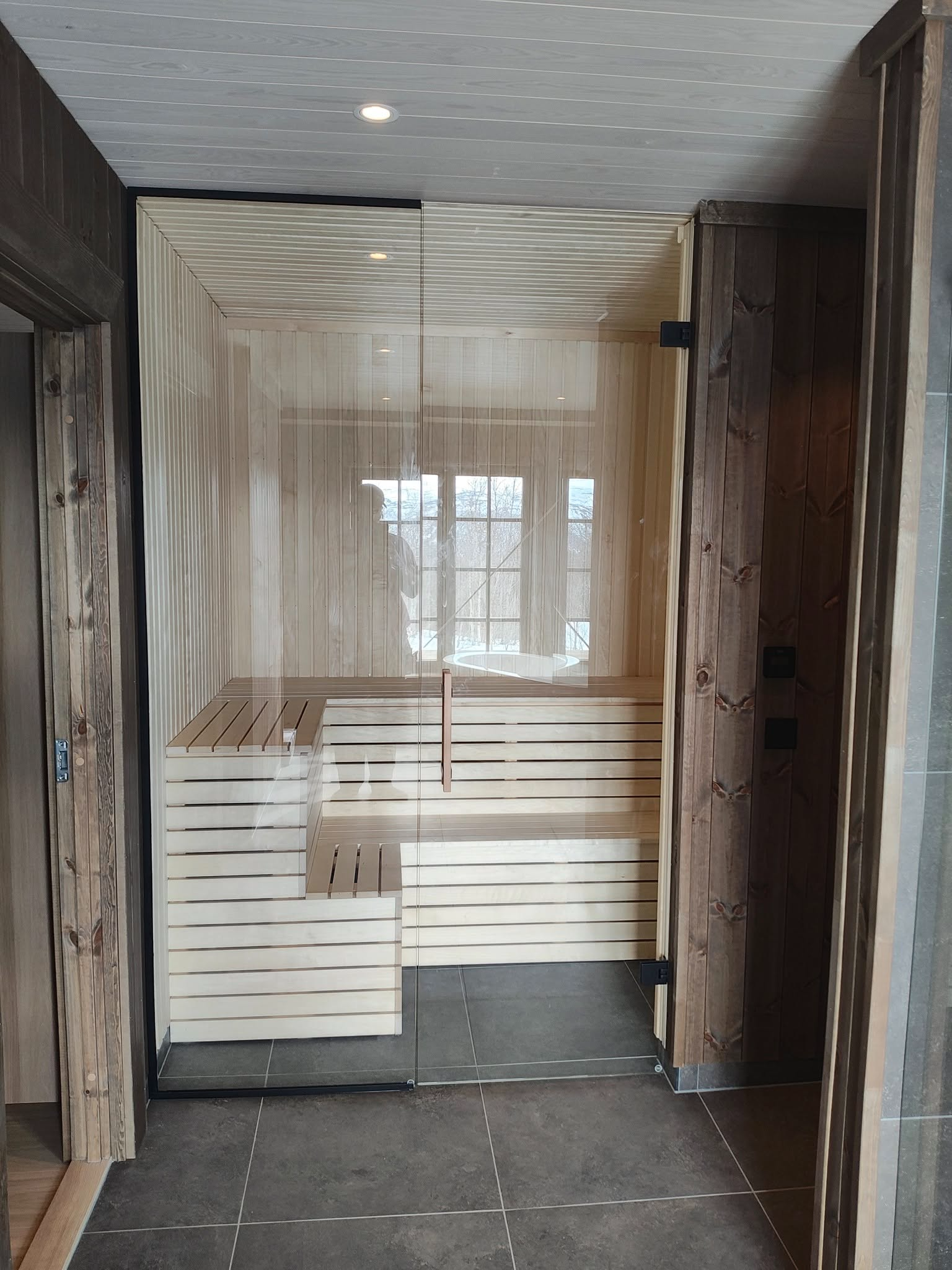 Moderne sauna med glassdør og trepanel, plassert i en stilren interiørsetting.
