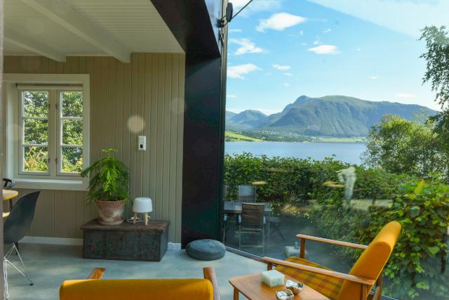 Lys stue med moderne møbler og utsikt over fjorden og fjellene i bakgrunnen.