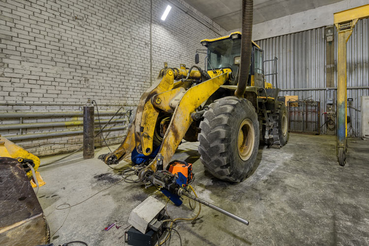 En stor gult gravemaskin står i en verksted med betongvegger og verktøy rundt.