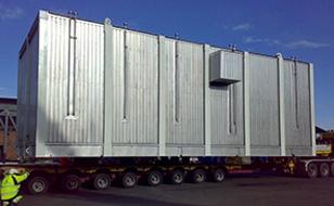 En stor, sølvfarget container på en lastebil, plassert på en industriell bakgrunn under blå himmel.