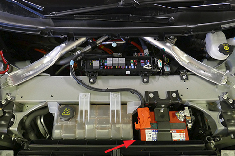 Bilde av motorrommet i en bil med batteri, sikringsboks og ledninger synlige.