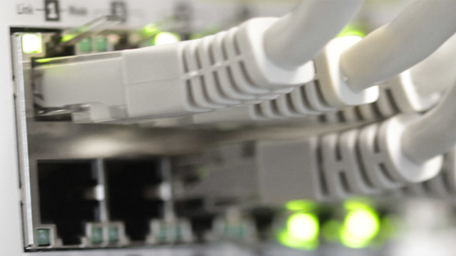 Nærbilde av nettverkskabler koblet til en switch med grønne lys som indikerer tilkobling.