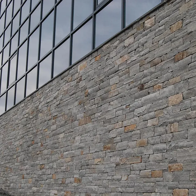 En moderne bygning med en grå steinvegg og store vinduer som reflekterer himmelen.