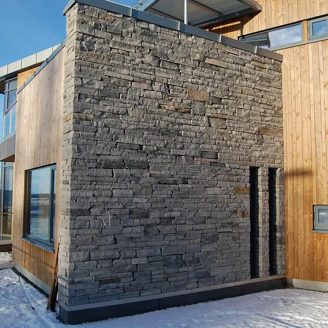 Moderne hus med steinvegg og trepanel, beliggende i snødekt landskap.