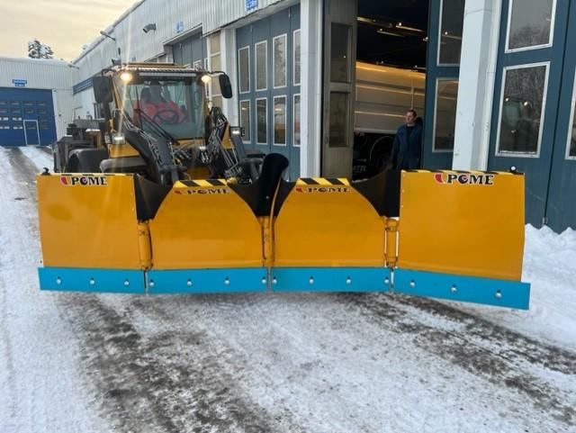 En stor snøplog i gult og blått foran en bygning, med en traktor som står klar til å rydde snø.
