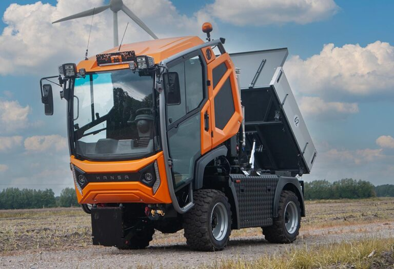 En oransje tippbil står på en grusvei med en vindmølle i bakgrunnen og en åpen tippkasse.