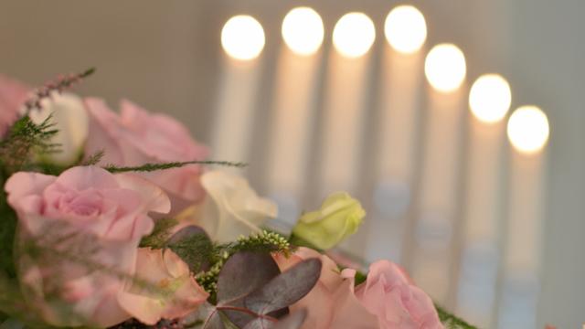 En bukett med rosa roser og grønne blader foran flere tente lys i bakgrunnen.