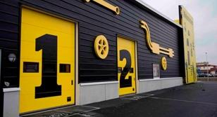 Fargerik bygning med svarte vegger og gule dører, dekorert med store verktøy og tallene 1 og 2.