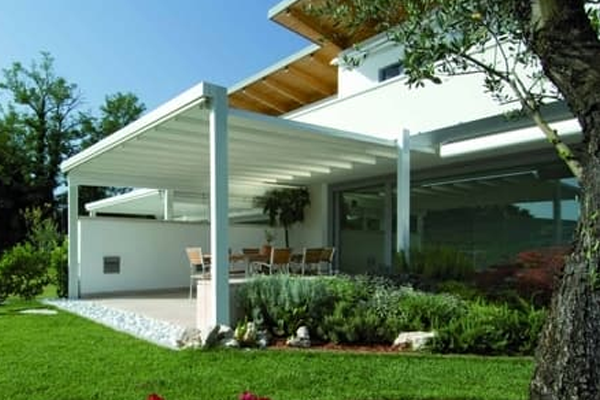 Moderne hus med terrasse, grønne planter og sitteplasser under pergolaen i hagen.