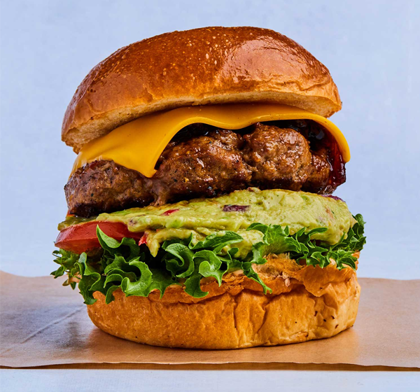 Saftig hamburger med cheddarost, guacamole, salat og tomat på en myk bolle.