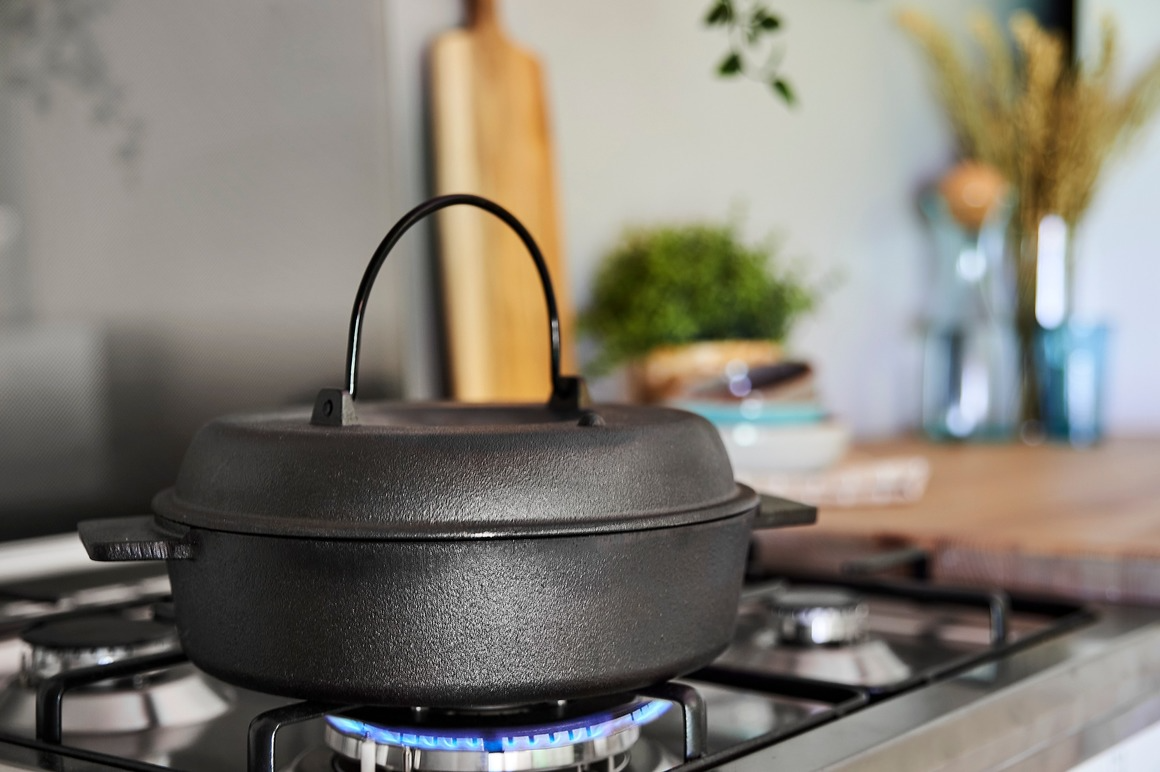 En svart gryte på en gasskomfyr med flamme, med en moderne kjøkkeninnredning i bakgrunnen.