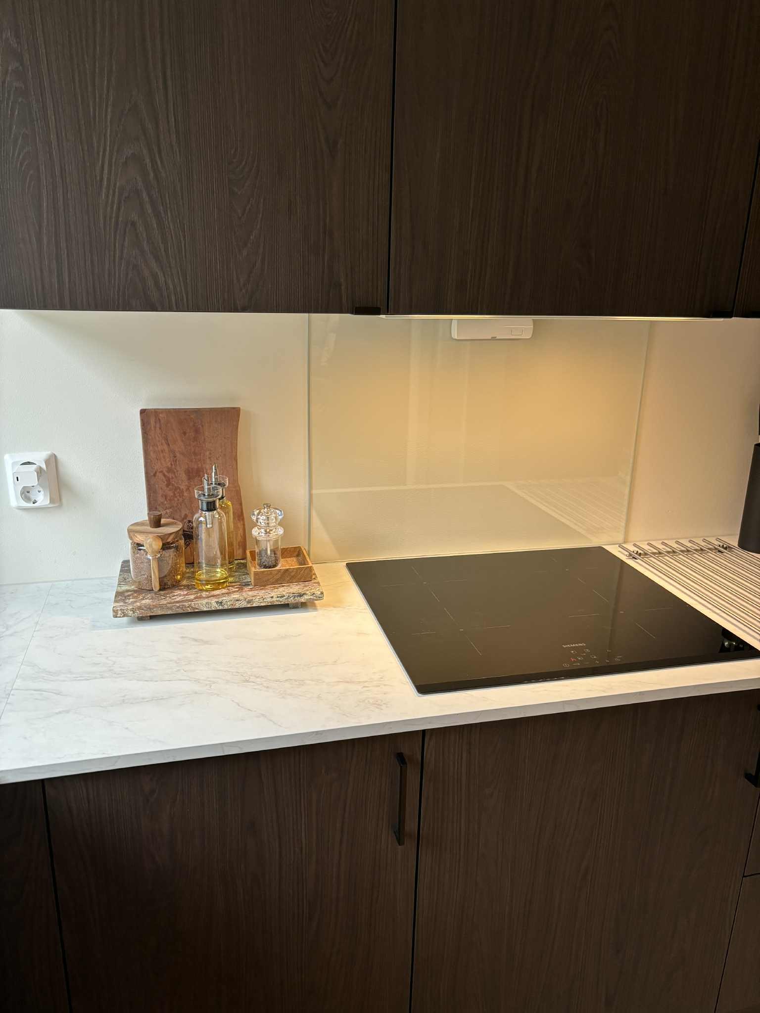 Moderne kjøkkenbenk med marmoroverflate, glassvegg og oljer i glassflasker på en trebrett.