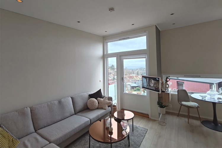 Moderne stue med lys sofa, glassbord og vindu som gir utsikt over byen.