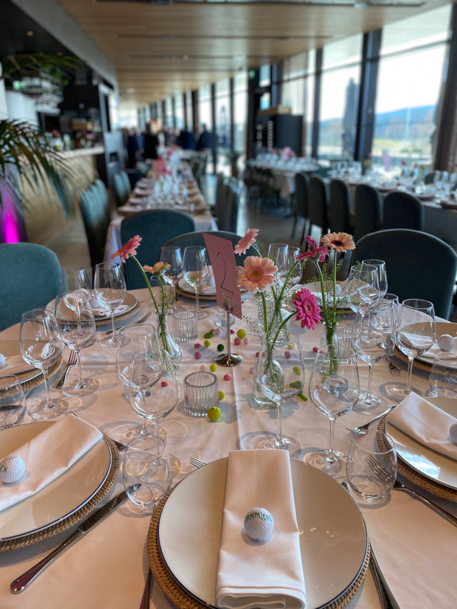 Elegant dekket bord med blomster, glass og servietter i en moderne restaurant med utsikt.