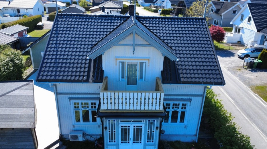 En moderne, hvit trehus med svart tak og balkong, beliggende i et rolig nabolag.