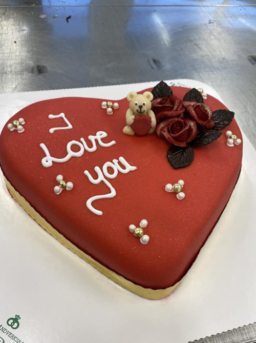 Hjertekake med rød marsipan, tekst "I Love You", en liten bjørn og roser som dekorasjon.