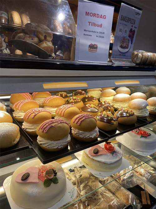 Fristende kaker og boller utstilt i en bakeri, med skilt om mandagstilbud.