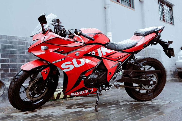 Rød Suzuki motorsykkel parkert på en gate med snø på setet og dekkene.