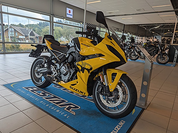 En gul Suzuki motorsykkel utstilt i en butikk med flere motorsykler i bakgrunnen.