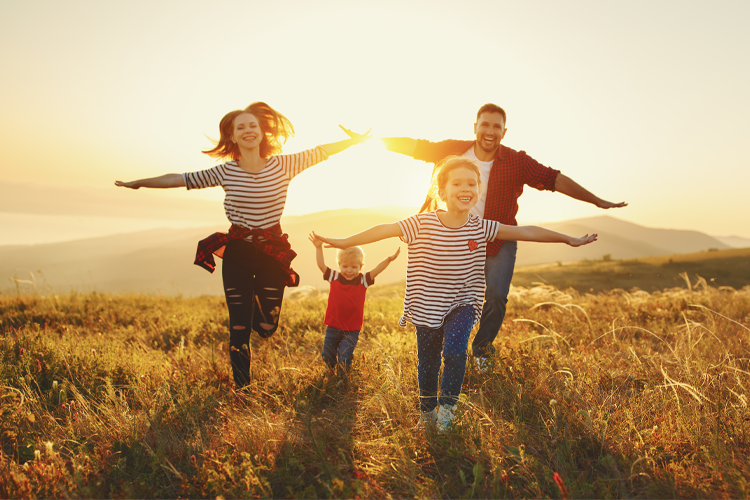 Familie som løper sammen i en eng med solnedgang, iført stripete skjorter og smilende ansikter.