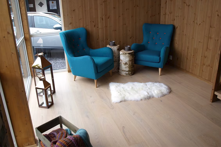 Koselig stue med to blå stoler, et teppe av saueskinn og en liten lampe på et trebord.