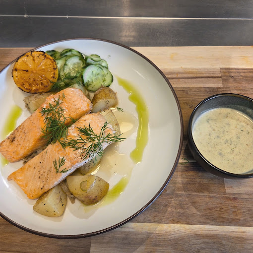 Laks med poteter, agurk og grillet sitron, servert med en kremet saus i en skål.