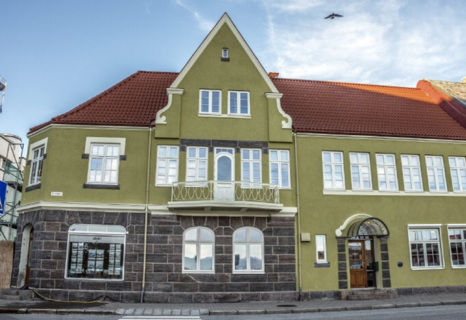 En stor, grønn bygning med rød tak og mange vinduer, beliggende på en gate.
