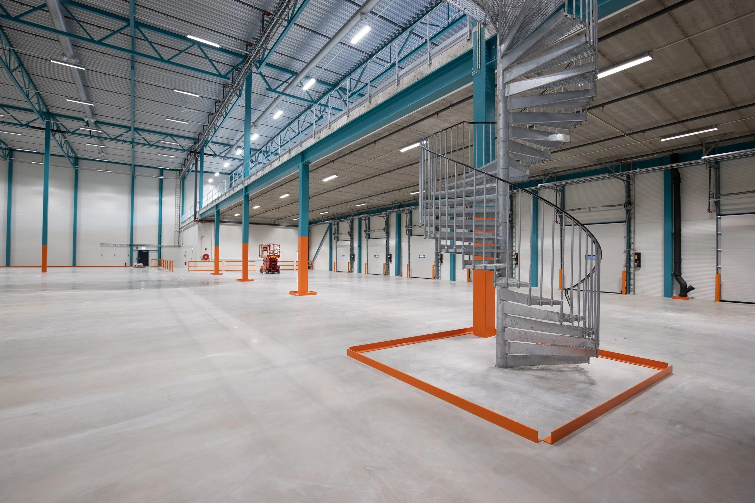 Lagerlokale med spiraltrapp, høyt tak og oransje detaljer på søylene og gulvet.