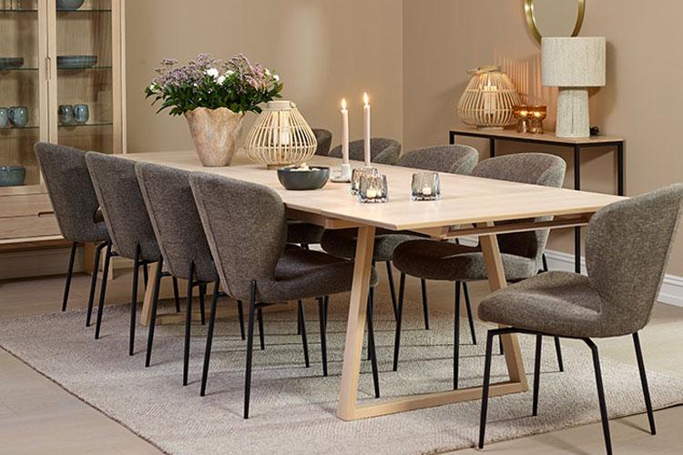 Moderne spisestue med et langt bord, grå stoler, lysestaker og blomsterdekorasjon.